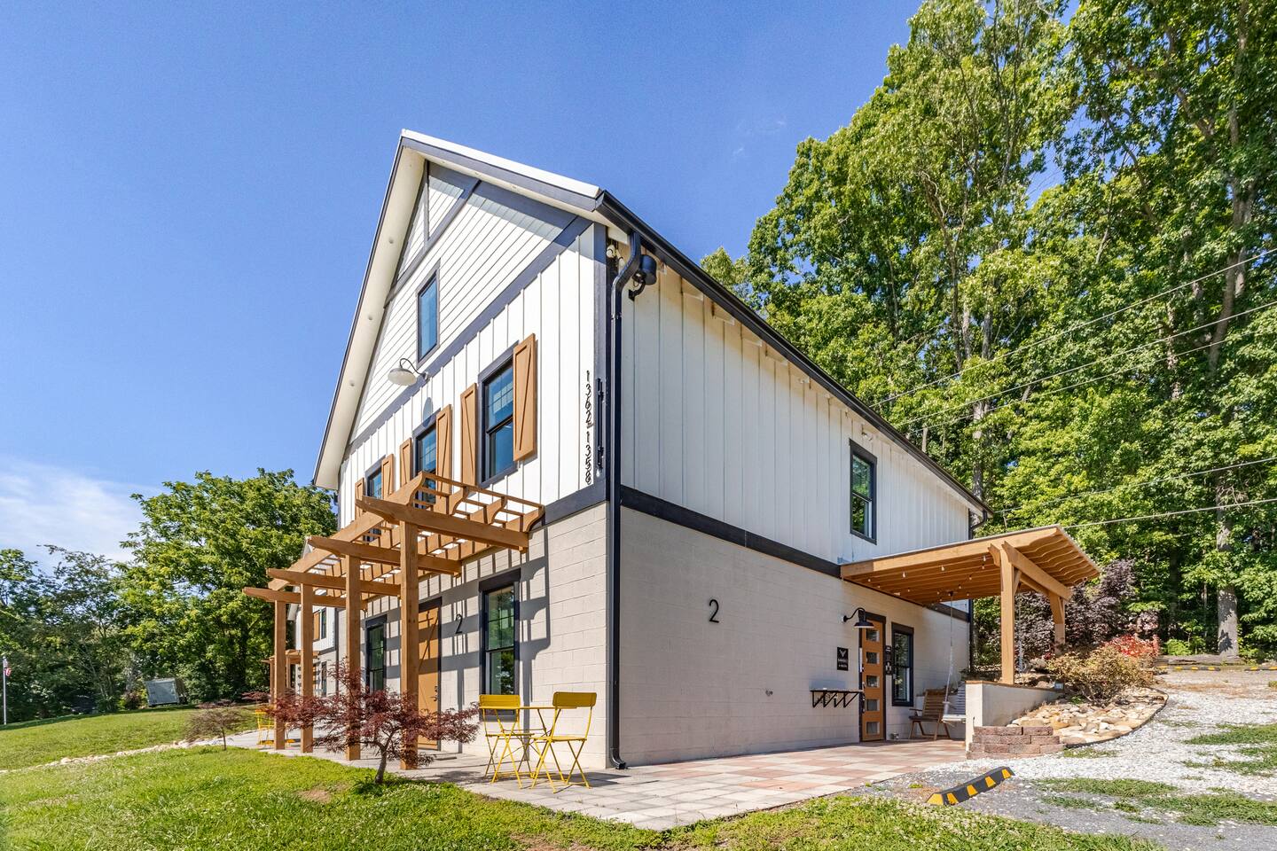 Modern farmhouse exterior with pergola, patio seating, and wooded privacy